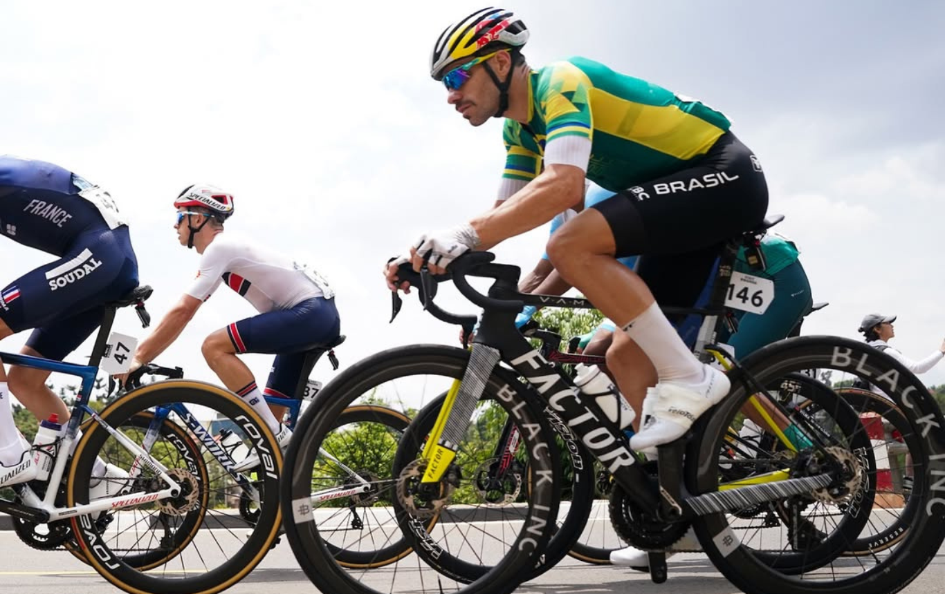 Ciclista em uma trilha com a bicicleta na mão, dentro de uma cabine telefônica abandonada.